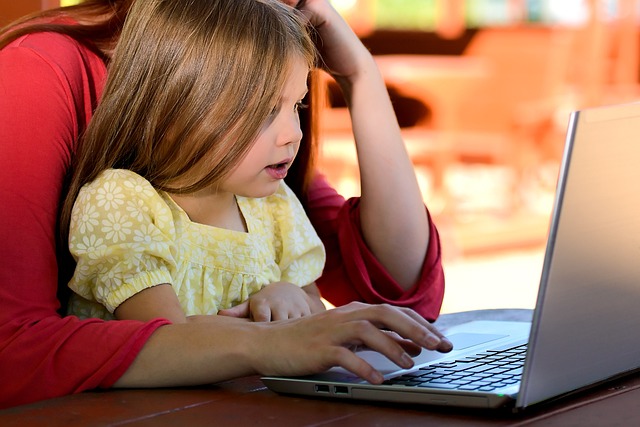 Frau arbeitet am Computer. Sie hat ihre Tochter auf dem Schoß