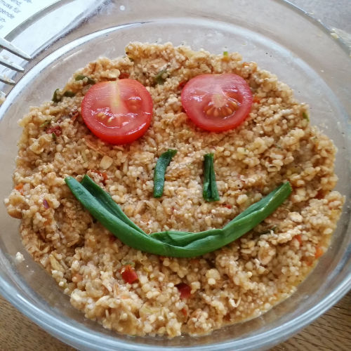 Schüssel mit Couscous auf den meine Tochter einen Smiley aus Tomatenn und Lauchzwiebeln legte